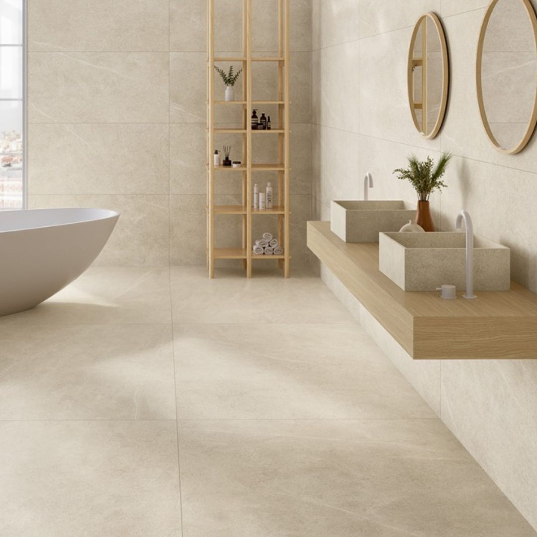 bathroom with large beige stone-effect wall and floor tiles, freestanding bath, double vessel sinks and floating wooden vanity