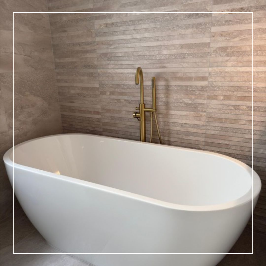 Modern bathroom featuring textured beige ceramic wall tiles behind a freestanding white bath, complemented by brushed brass floor-mounted tap for a warm contemporary look.