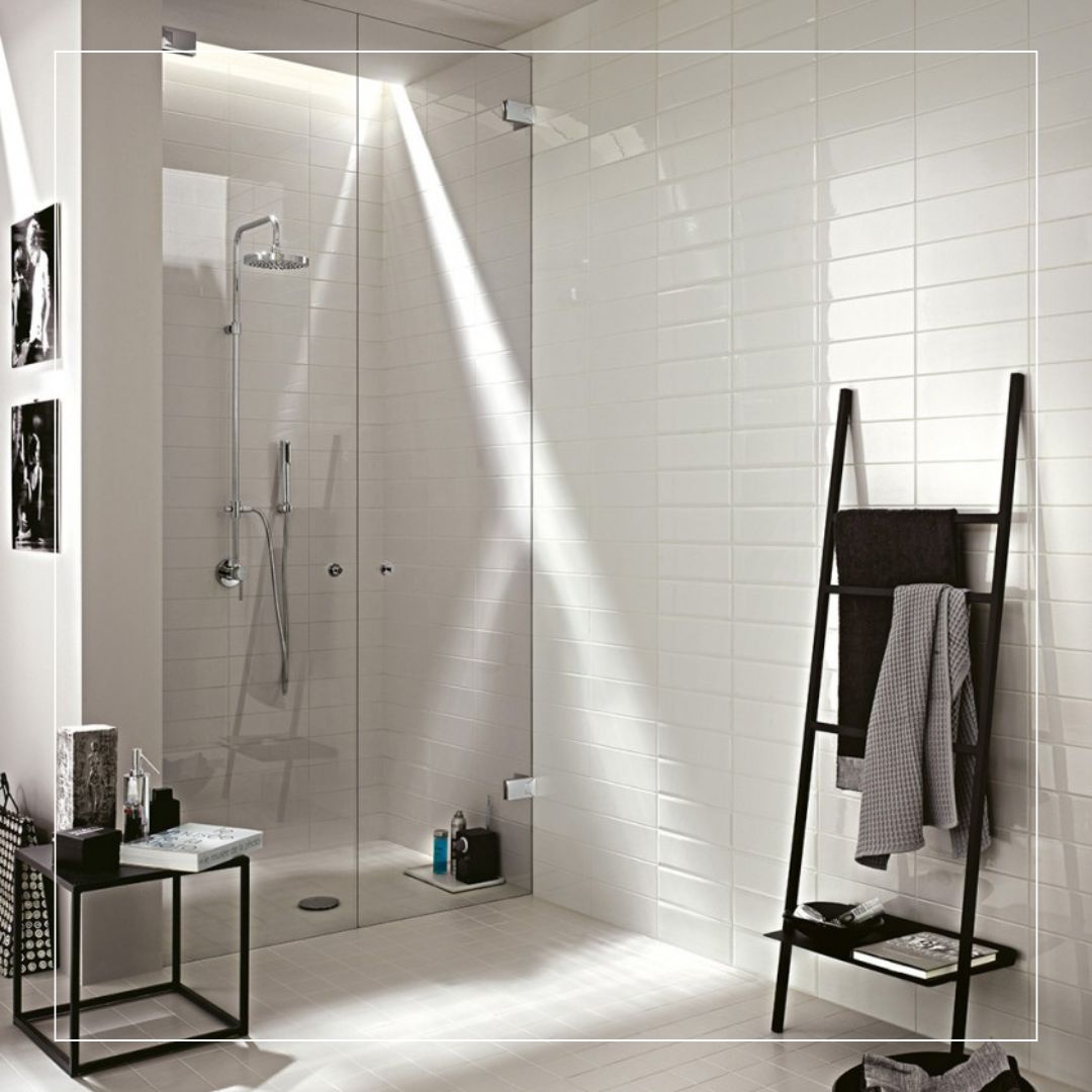 Minimalist bathroom with glossy white ceramic wall tiles in a subway style, paired with a walk-in glass shower and light ceramic floor tiles for a clean modern finish