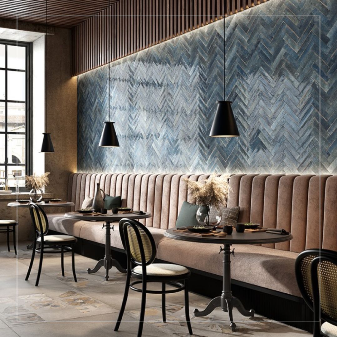 Restaurant interior featuring blue-grey herringbone wall tiles with subtle tonal variation, paired with warm beige floor tiles