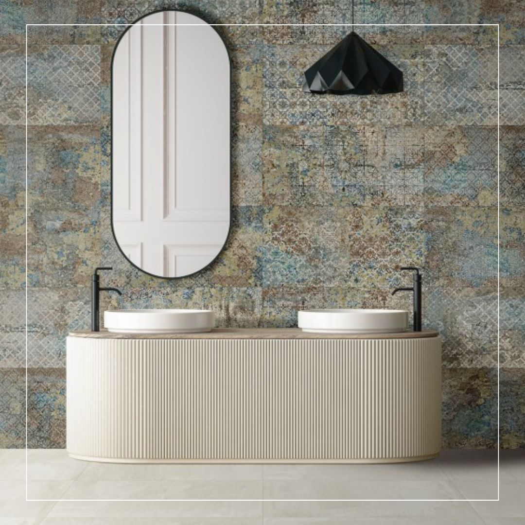 Bathroom wall finished with patterned tiles in muted blue, grey, and warm beige tones, creating a softly layered, vintage-inspired backdrop that pairs with a cream vanity and matte black fixtures