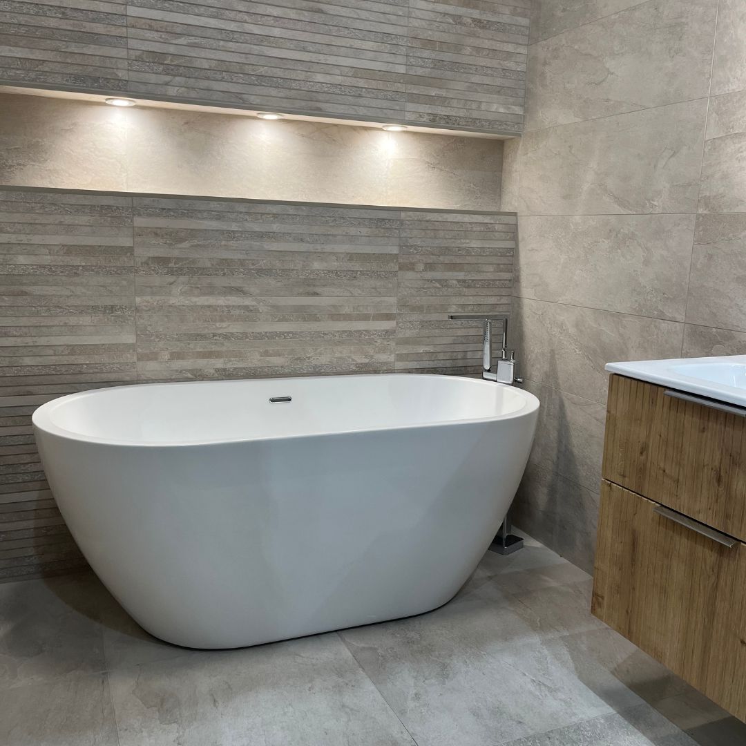 Warm neutral bathroom with grey stone-effect tiles, textured feature wall, freestanding bath, wood vanity unit and soft recessed lighting