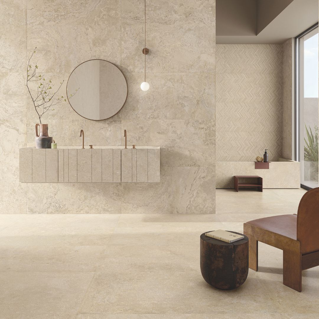 Warm neutral bathroom with large beige stone-effect tiles, floating double vanity unit, round mirror and textured feature wall