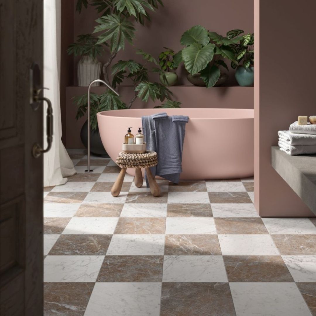 Warm neutral bathroom with blush pink freestanding bath, chequered stone-effect floor tiles, mauve walls and indoor plants