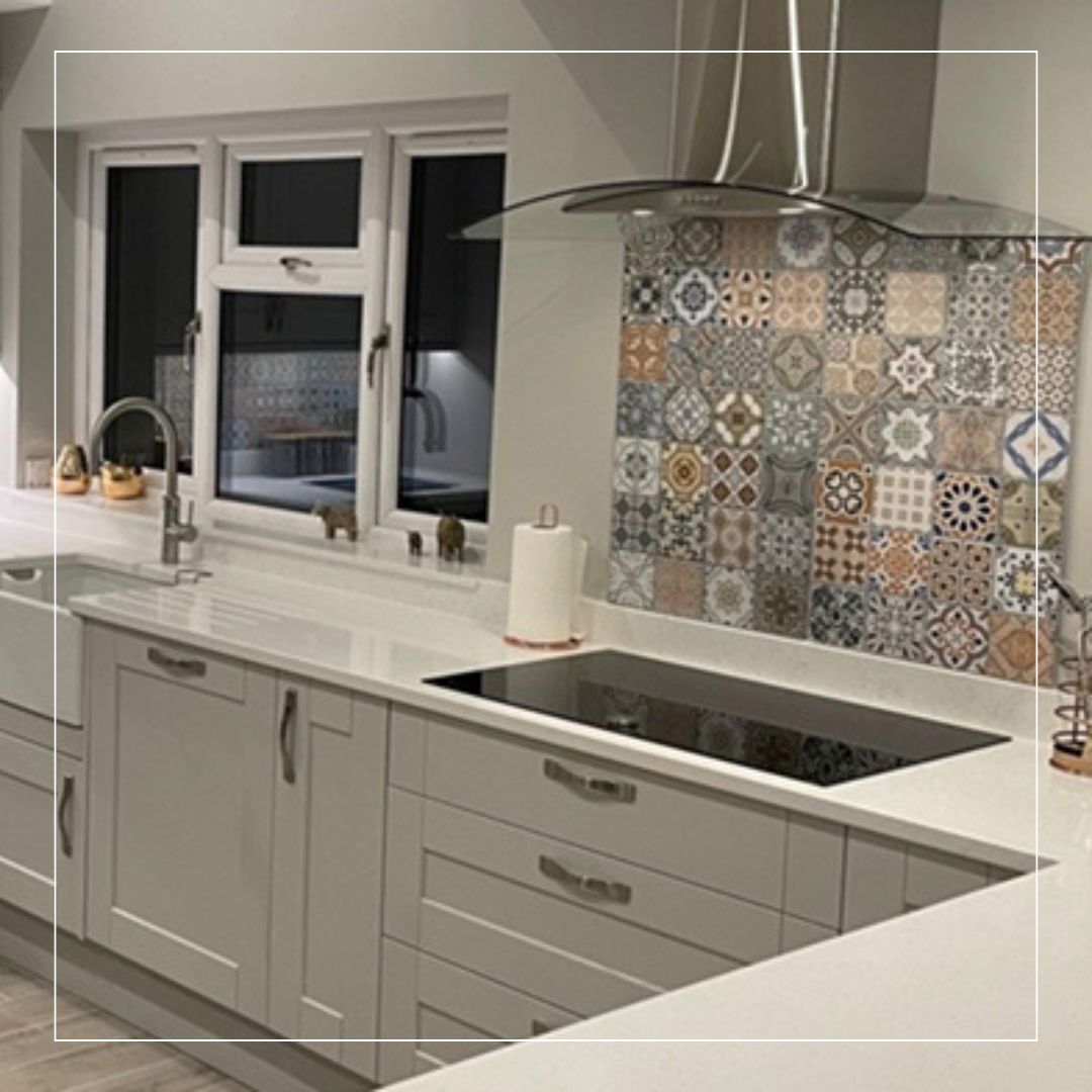 Modern kitchen with white cabinets and colourful patterned tile splashback behind hob