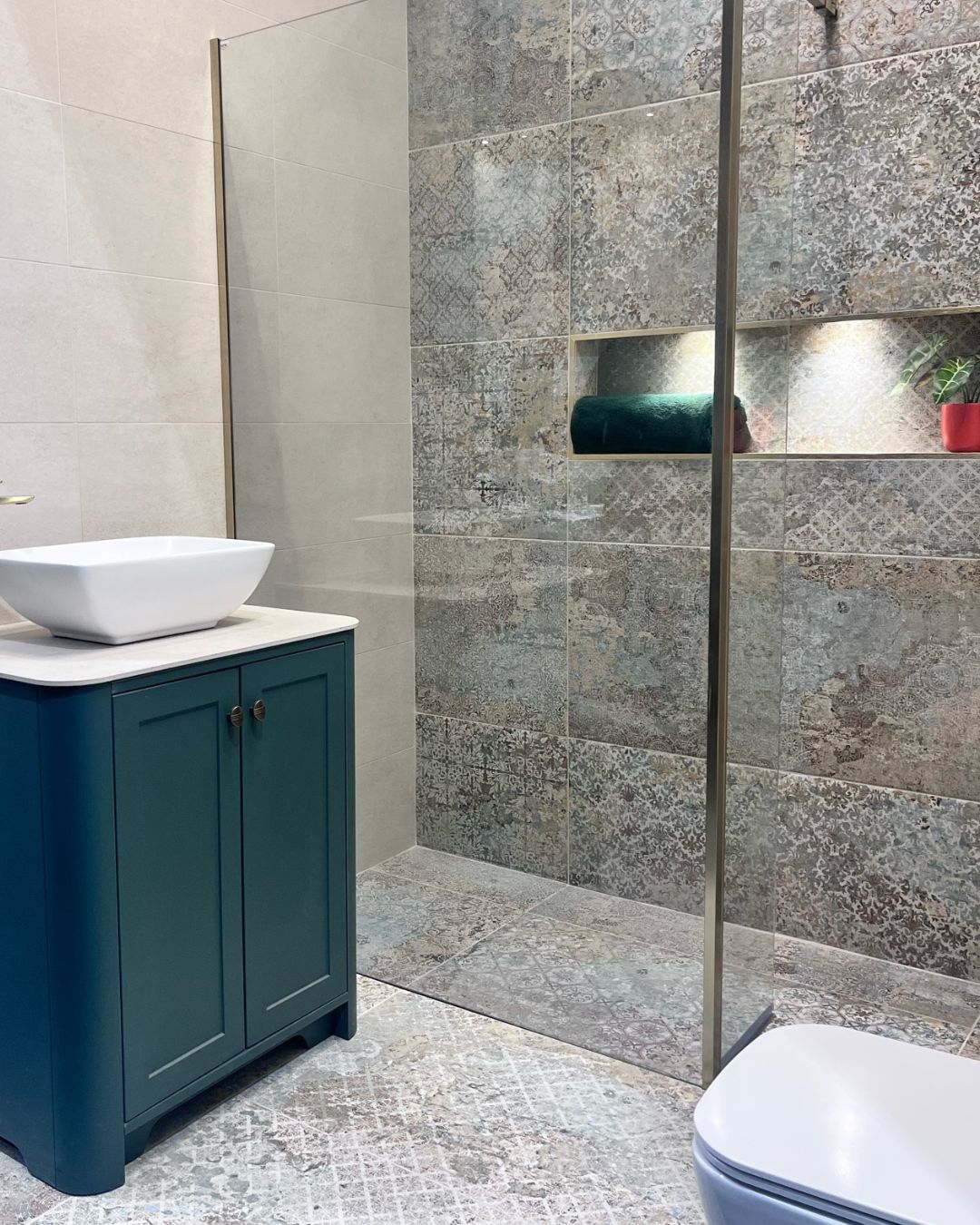 Wet room with grey patterned floor and shower wall tiles, walk-in shower with glass screen and dark teal vanity unit