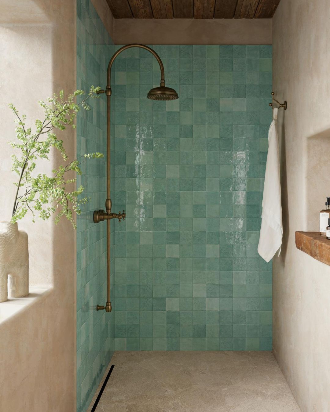 Walk-in wet room with green square wall tiles, beige stone-effect flooring, brass rainfall shower and linear floor drain.